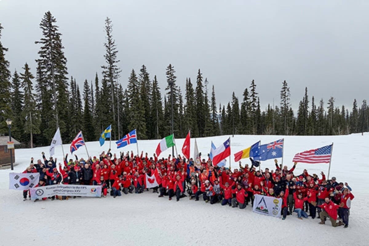 Десятки участников конгресса в красных куртках позируют для групповой фотографии на заснеженной горнолыжной трассе. Делегации держат флаги своих стран — Южной Кореи, Швеции, Великобритании, Италии, Канады, Чили, Австралии, США и других. На фоне — ели и пасмурное зимнее небо