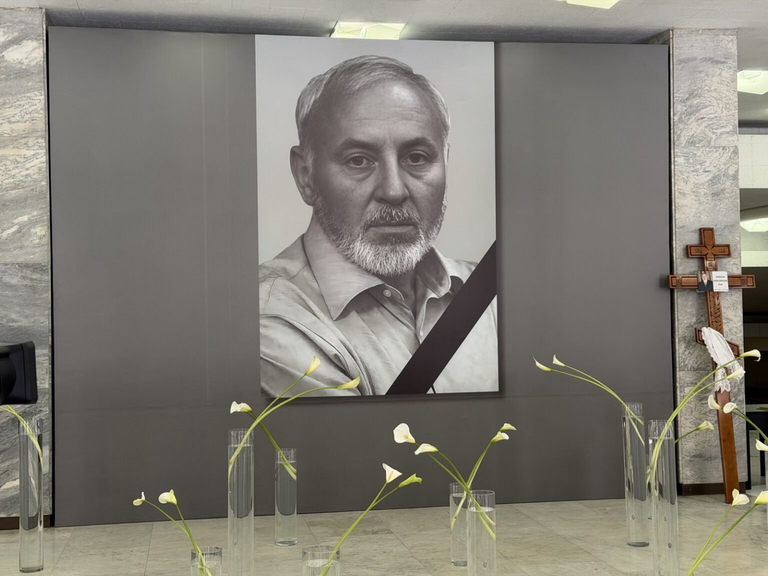 Траурный чёрно-белый портрет Георге Урски с траурной лентой в Национальном дворце Николае Сулак, белые каллы на переднем плане