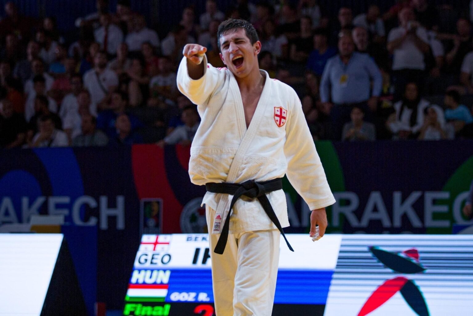 Грузинский дзюдоист в белом кимоно эмоционально празднует победу в финальном поединке