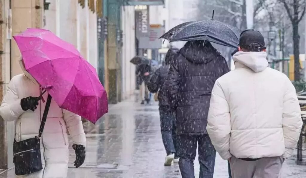 Пешеходы с зонтами идут по городской улице во время сильного снегопада и дождя