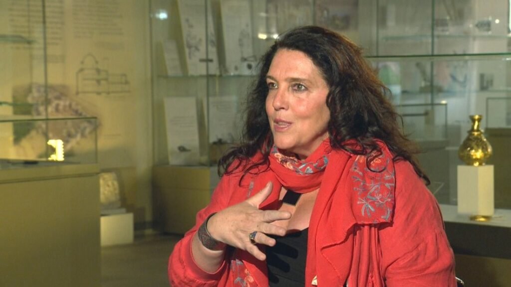 Бетани Хьюз в красном шарфе беседует на фоне музейных витрин