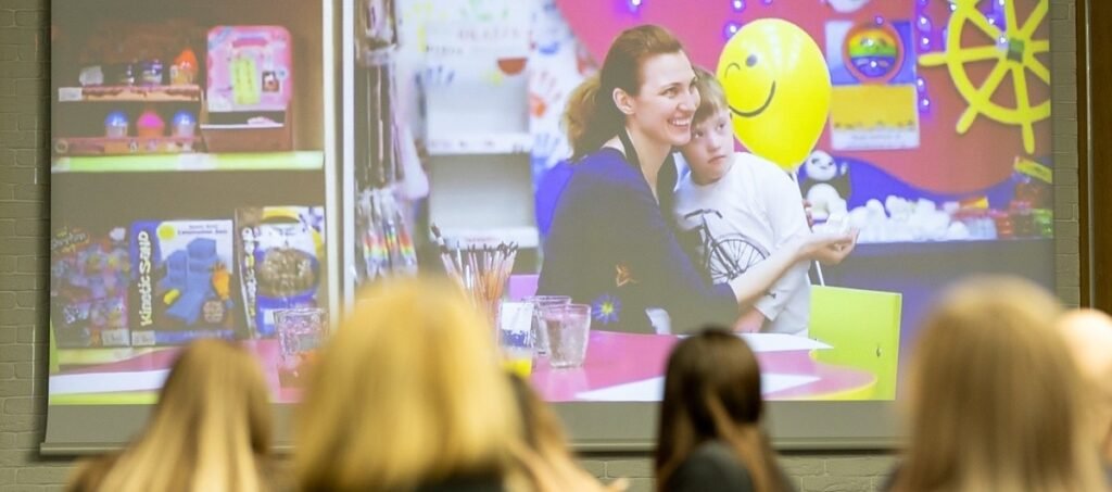 Зрители наблюдают за презентацией на конференции по здоровью мозга в Молдове, на экране &mdash; женщина с ребёнком в игровой комнате