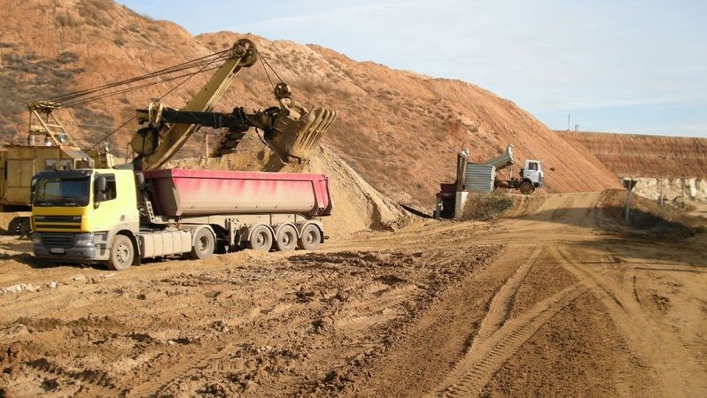Экскаватор загружает песок в грузовик на карьере — промышленная добыча песка и гравия в открытом разрезе