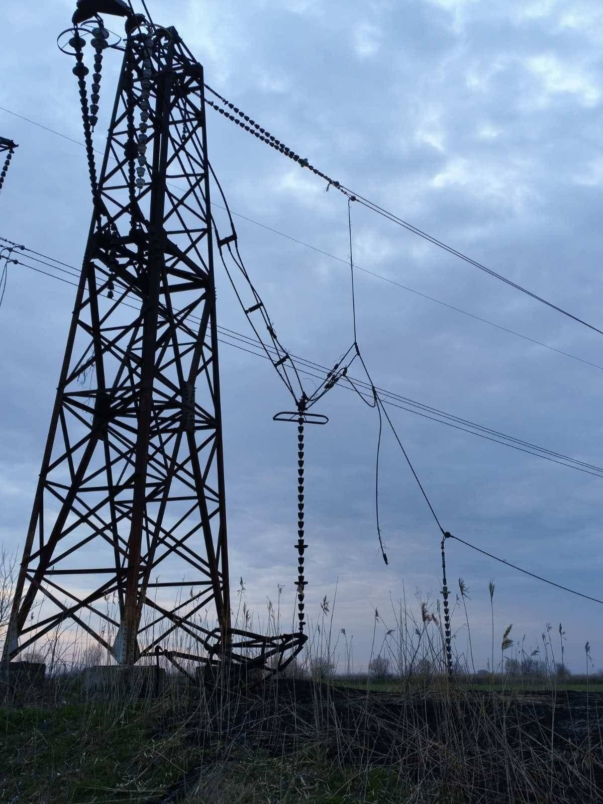 Повреждённая опора высоковольтной линии электропередачи с оборванными проводами на фоне пасмурного неба