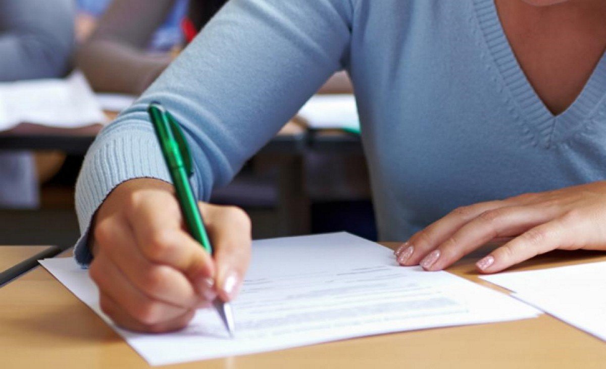 Ученица пишет письменный экзамен за партой в аудитории, держа зелёную ручку