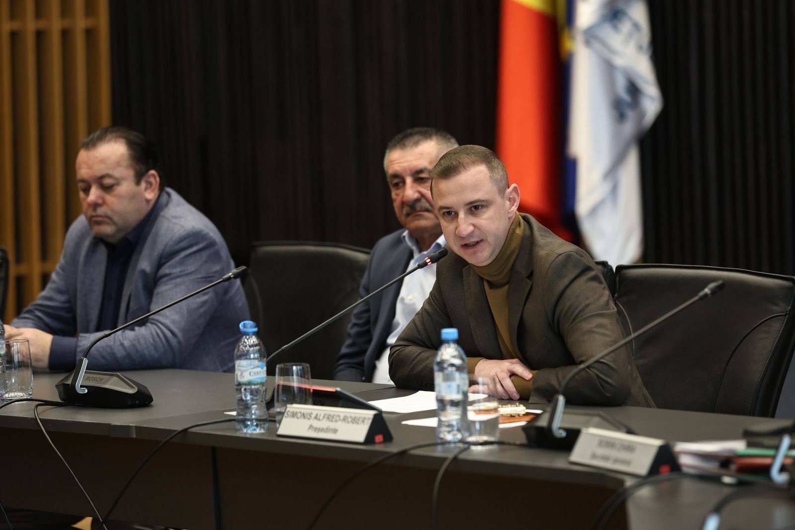 Чиновники за столом на заседании уездного совета Тимиш, на заднем плане — флаги Румынии и жудеца