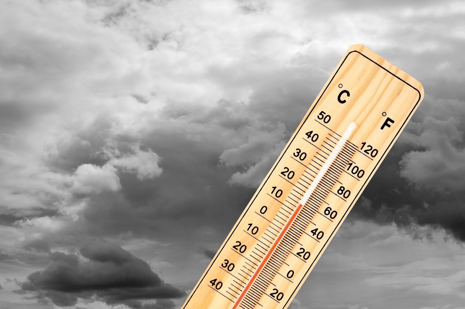 Деревянный термометр на фоне тёмных грозовых туч, символизирующий резкое понижение температуры