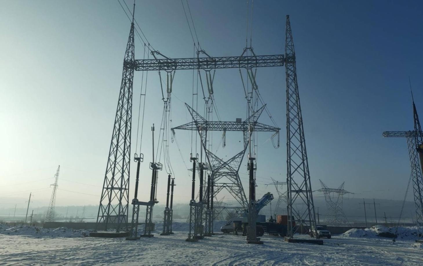 Строительство энергетической инфраструктуры ЛЭП зимой: опоры линии электропередачи и оборудование на заснеженной площадке