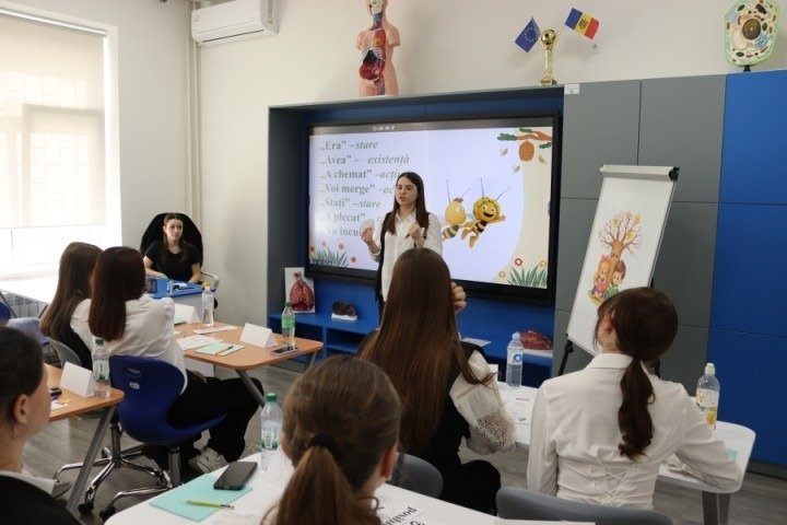 Молодая учительница проводит урок румынского языка у интерактивной доски в рамках конкурса, участники наблюдают за презентацией