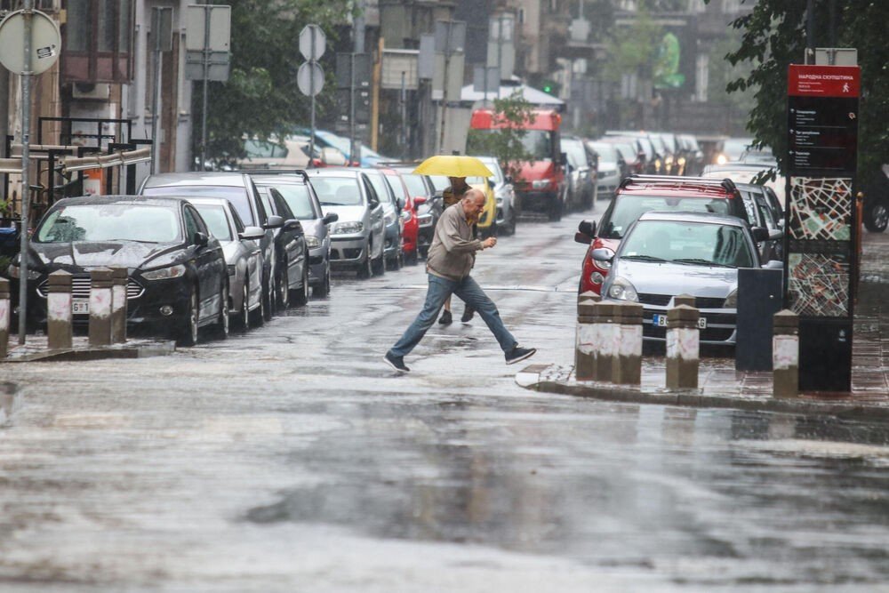 Мужчина с жёлтым зонтом перебегает улицу в дождь