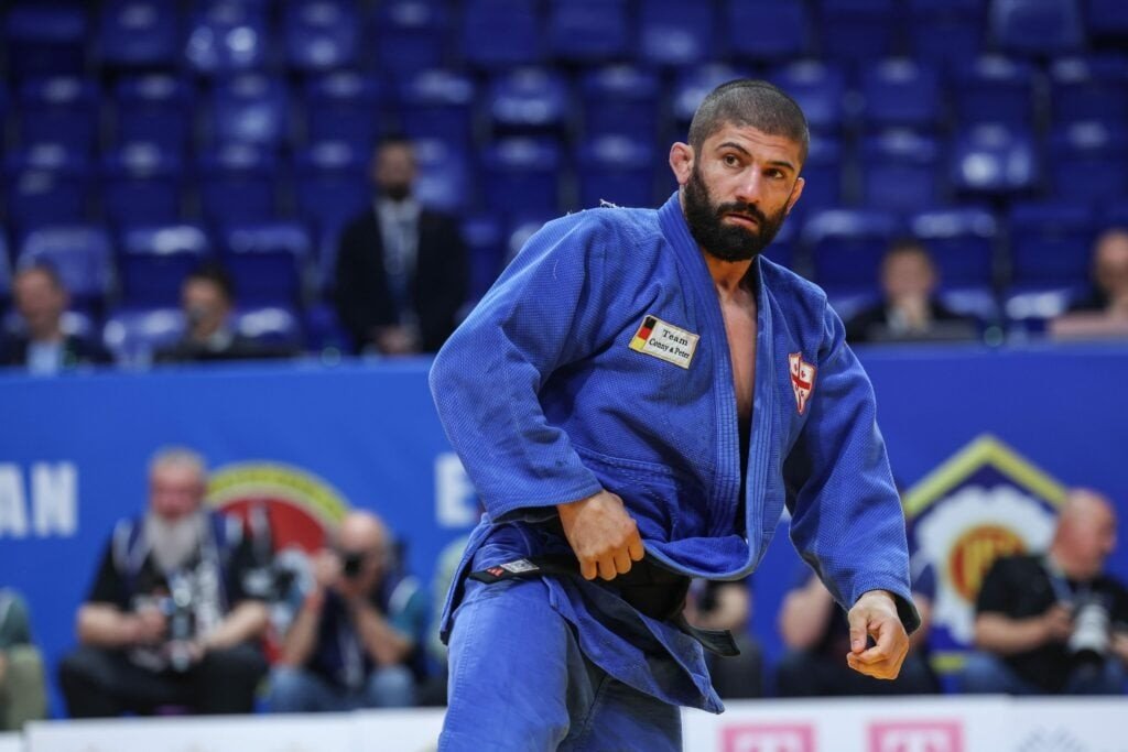 Грузинский дзюдоист в синем кимоно сосредоточенно готовится к схватке