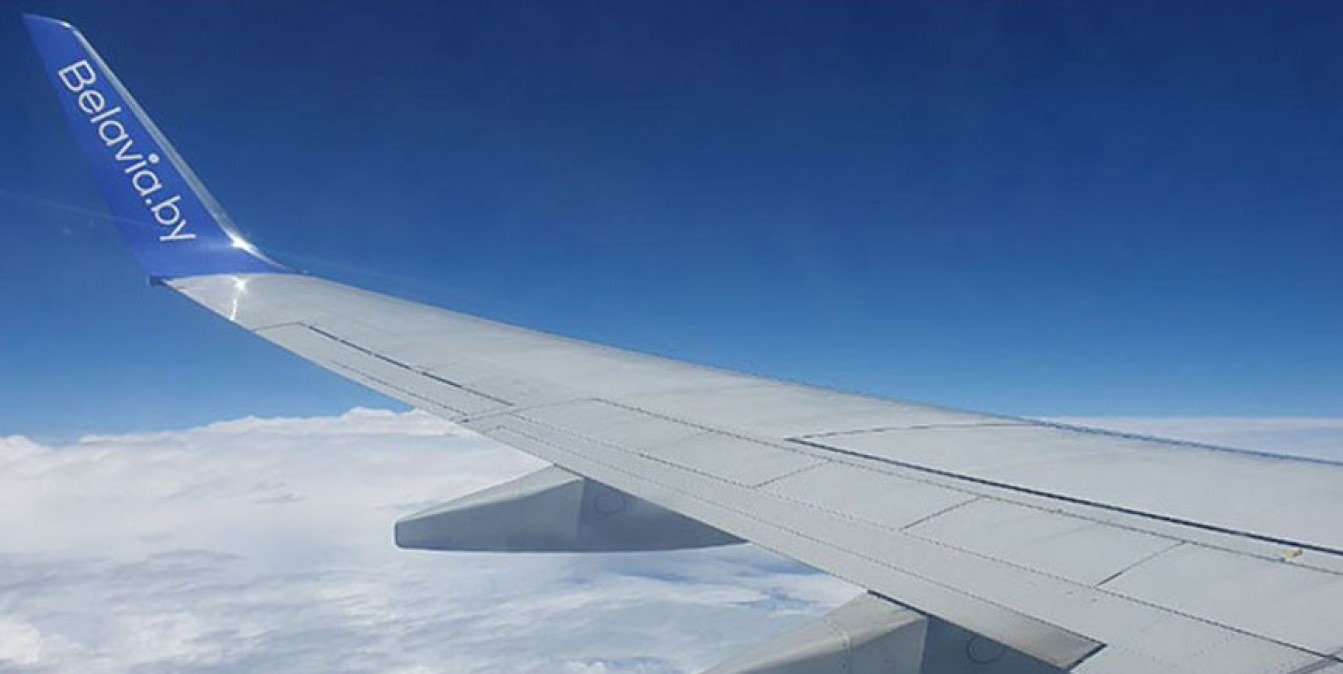 Вид на крыло самолёта «Белавиа» из иллюминатора на фоне голубого неба и облаков