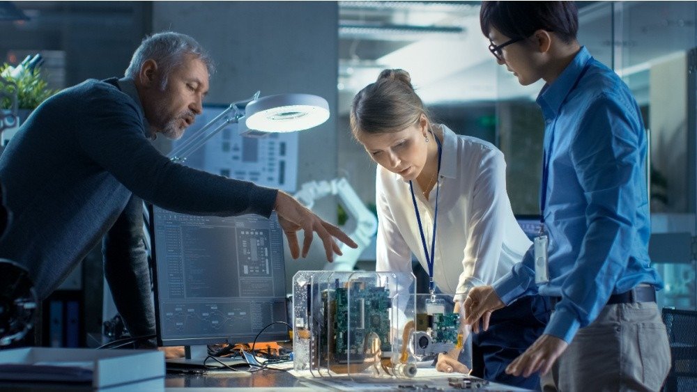 Три исследователя изучают прототип устройства в современной технологической лаборатории