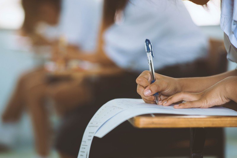 Треть школьников в Румынии не сдала пробный экзамен Ученица пишет экзаменационную работу в классе — крупный план руки с ручкой над листом бумаги