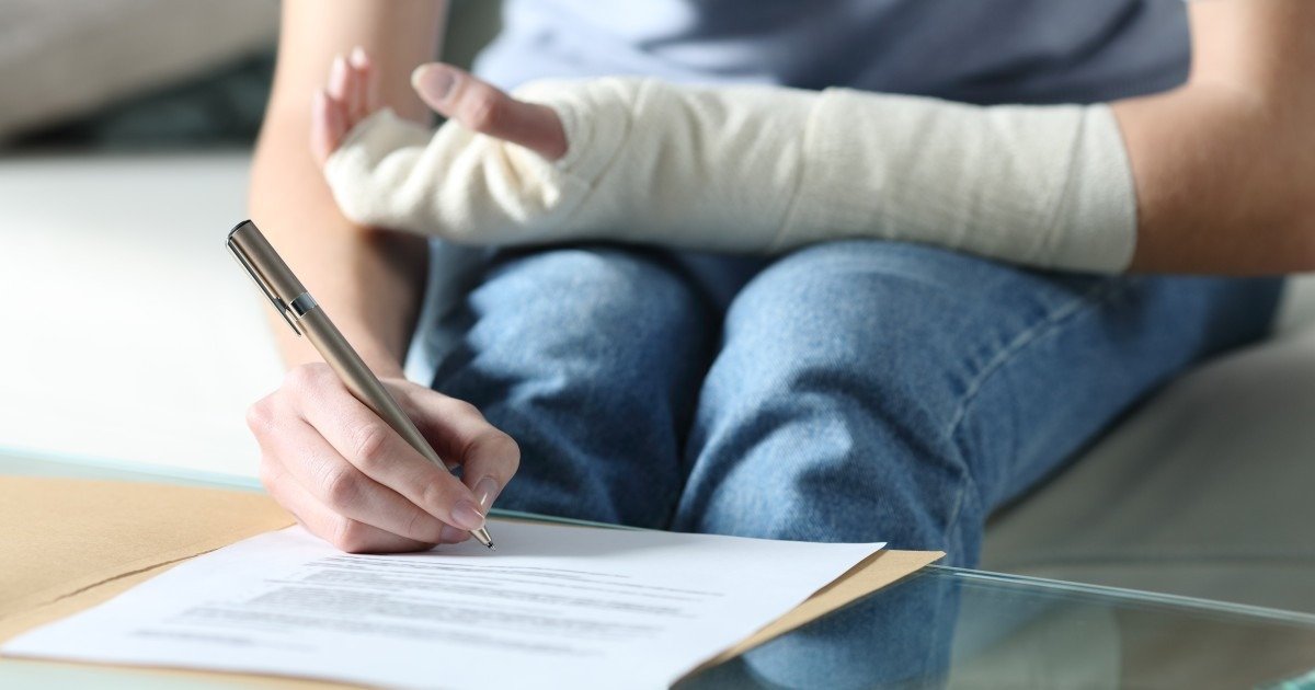 Человек с гипсом на руке подписывает документ