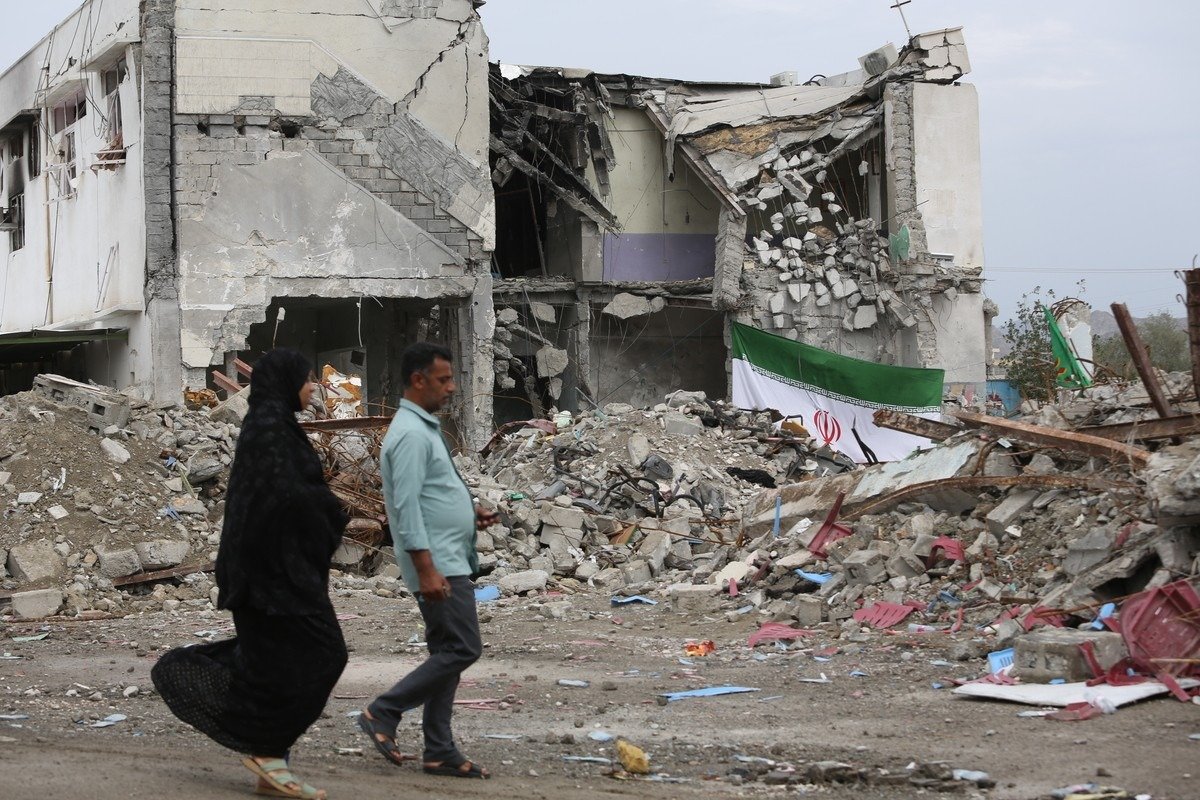 Мужчина и женщина идут мимо разрушенного здания среди обломков в иранском городе