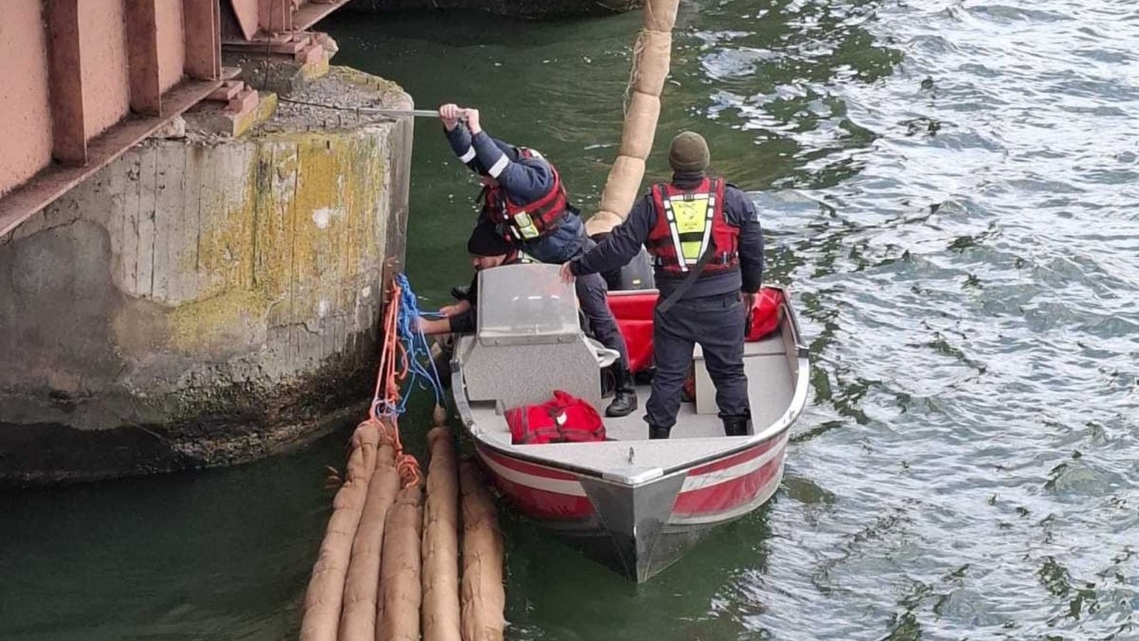 Спасатели с лодки закрепляют сорбентные боны у опоры моста через Днестр