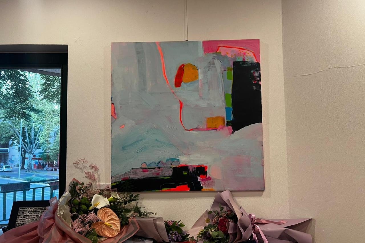 Большое полотно Ивоны Скочилич с пастельным фоном и контрастными красно-чёрными вставками — у стены клуба «Иво Андрич», а на полу букеты, подаренные художнице на открытии
