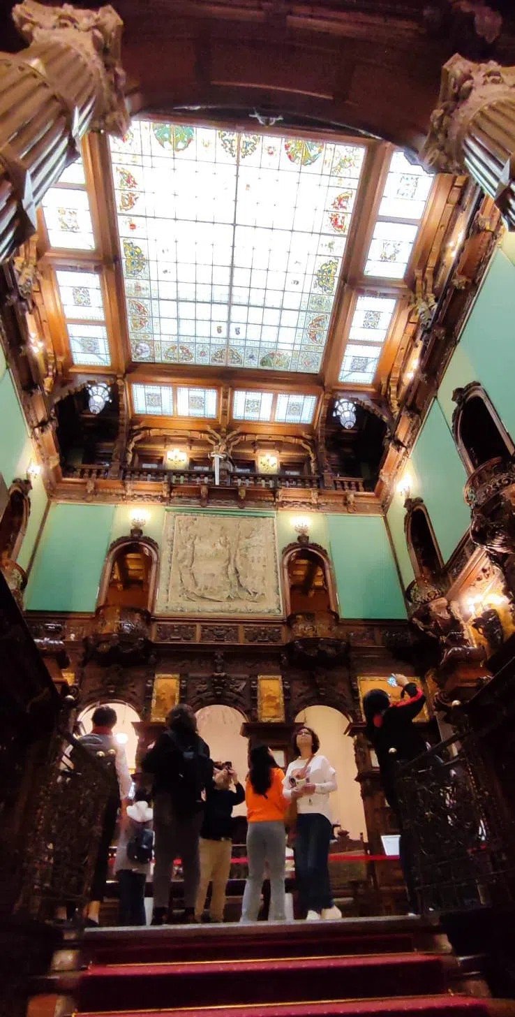 Парадный холл замка Пелеш с витражным потолком и туристами на мраморной лестнице