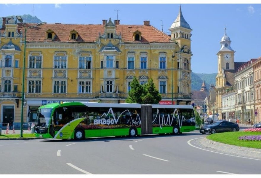 Электрический автобус RATBV с фирменной ливреей «Brașov» в историческом центре города на фоне гор