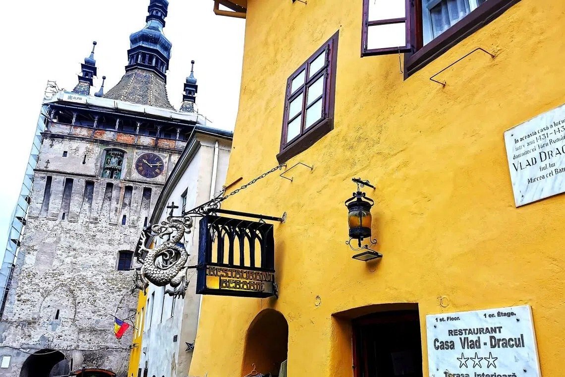 Часовая башня Сигишоары и жёлтый фасад дома «Casa Vlad Dracul» — предполагаемого места рождения Влада Цепеша