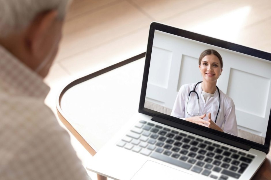 Пожилой мужчина перед ноутбуком с врачом на экране