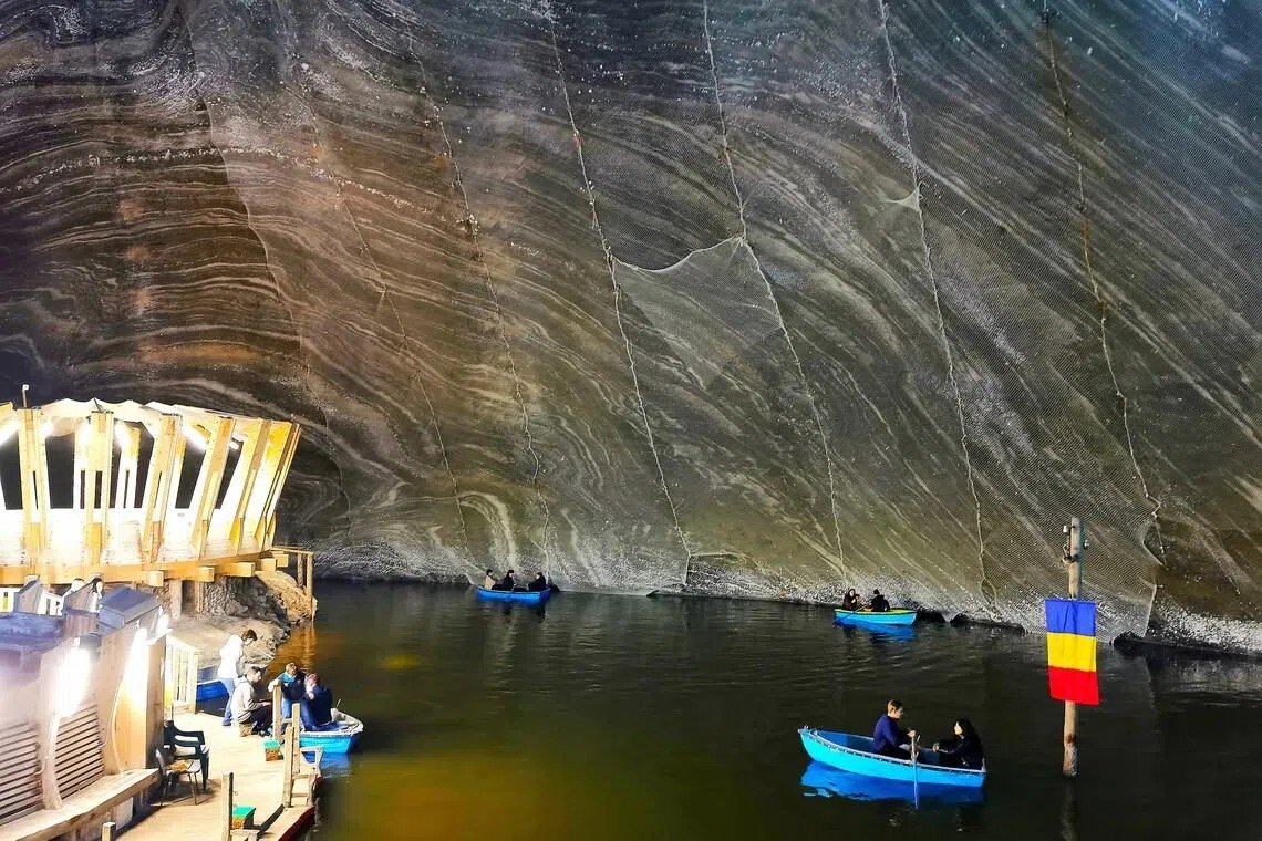 Подземное озеро соляной шахты Турда с синими лодками туристов и румынским флагом