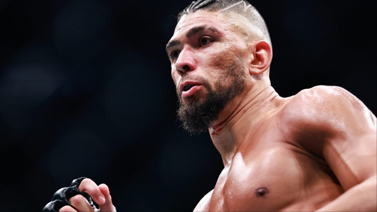 Джонни Уокер в октагоне UFC во время боя в полутяжёлом весе: бразилец сосредоточен, лицо в крови и поту, кулак сжат в перчатке