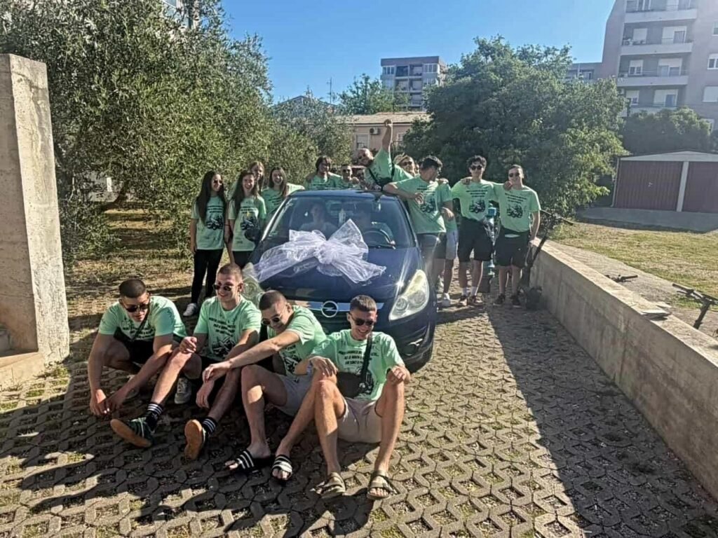 Задарские выпускники в зелёных футболках вокруг подаренного учительнице синего Opel Corsa