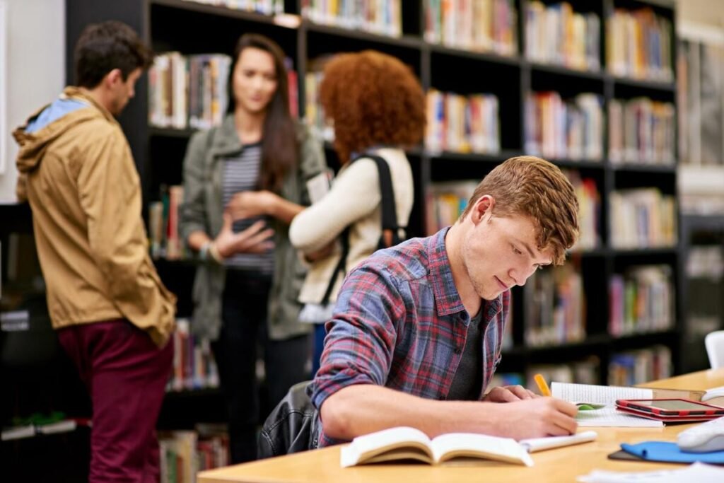 Студенты в университетской библиотеке за столом и у книжных стеллажей — иллюстрация к материалу о плате за обучение для иностранных студентов