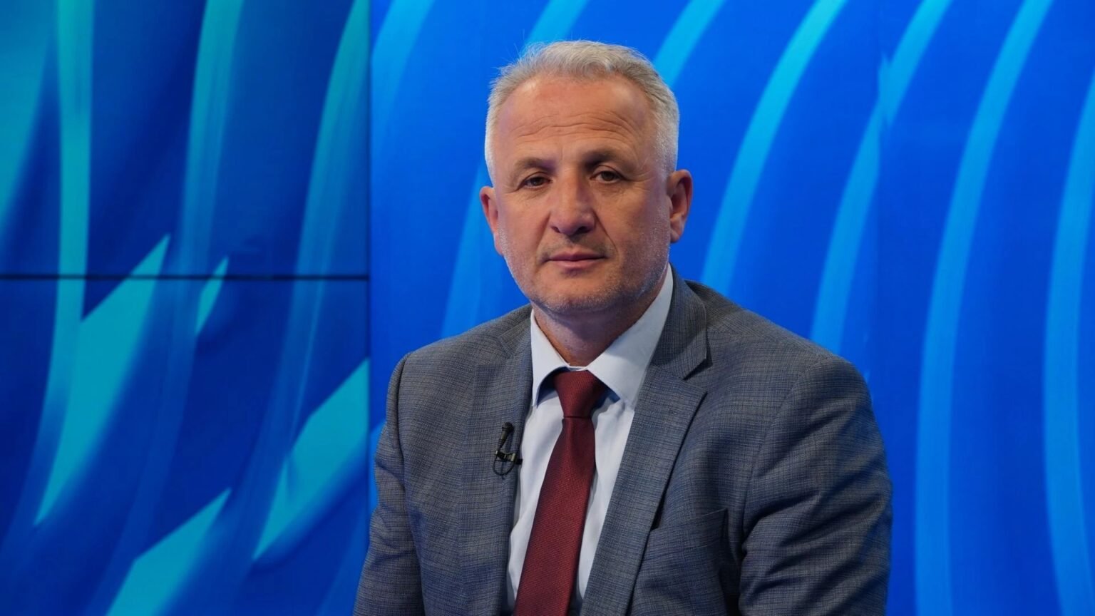 В Сараево пройдёт конференция памяти Расима Муминовича Мужчина средних лет с седыми волосами в сером пиджаке и бордовом галстуке сидит в синей телестудии с подсветкой логотипа Hayat