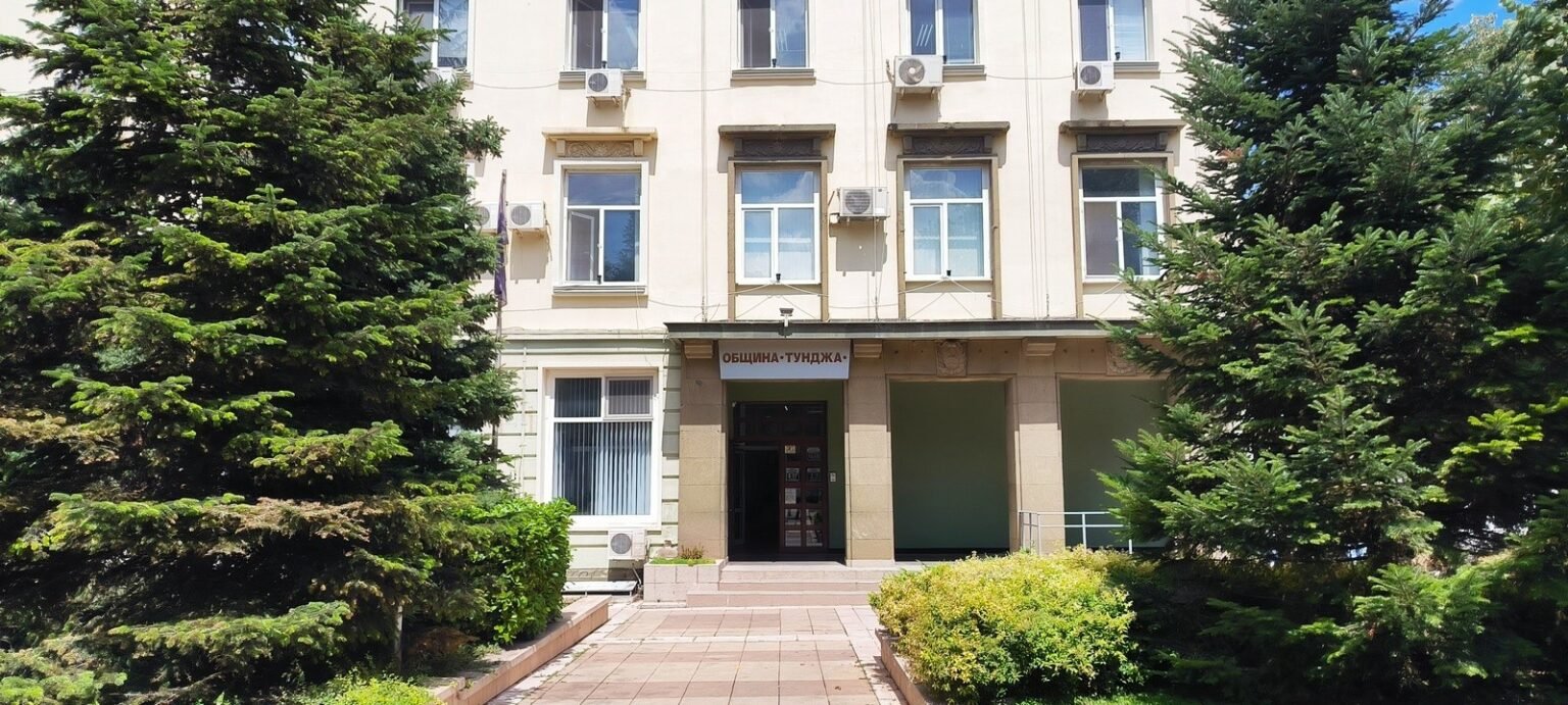 Тунджа: «Спасовден» и 100 лет читалища — программа недели Парадный вход административного здания общины Тунджа в окружении высоких хвойных деревьев в солнечный день