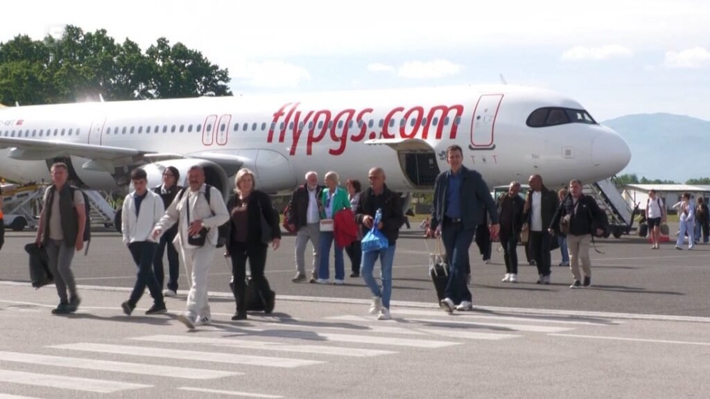 Пассажиры рейса Pegasus Airlines идут по перрону Международного аэропорта Тузла после прилёта; на фоне виден белый Airbus A320 с фирменной ливреей flypgs.com и зелёные холмы Боснии