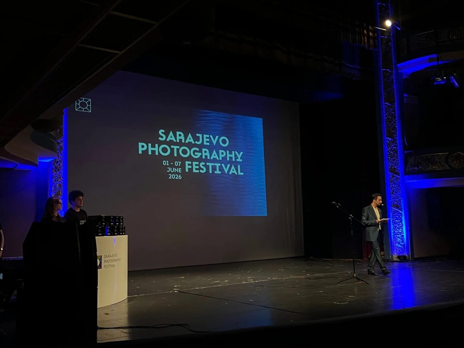 Сцена Народного театра в Сараево с проекцией логотипа Sarajevo Photography Festival 01–07 июня 2026 года; ведущий открывает церемонию награждения пятого юбилейного фотофестиваля