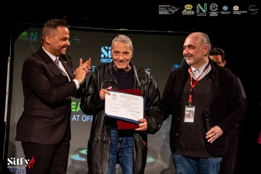 Драматург Андреас Стайкос получает диплом фестиваля Sitfy Georgia из рук художественного руководителя Мазена Эль-Чарабави (слева) и директора фестиваля Левана Хатагури (справа) на сцене Национального театра имени Шота Руставели в Тбилиси