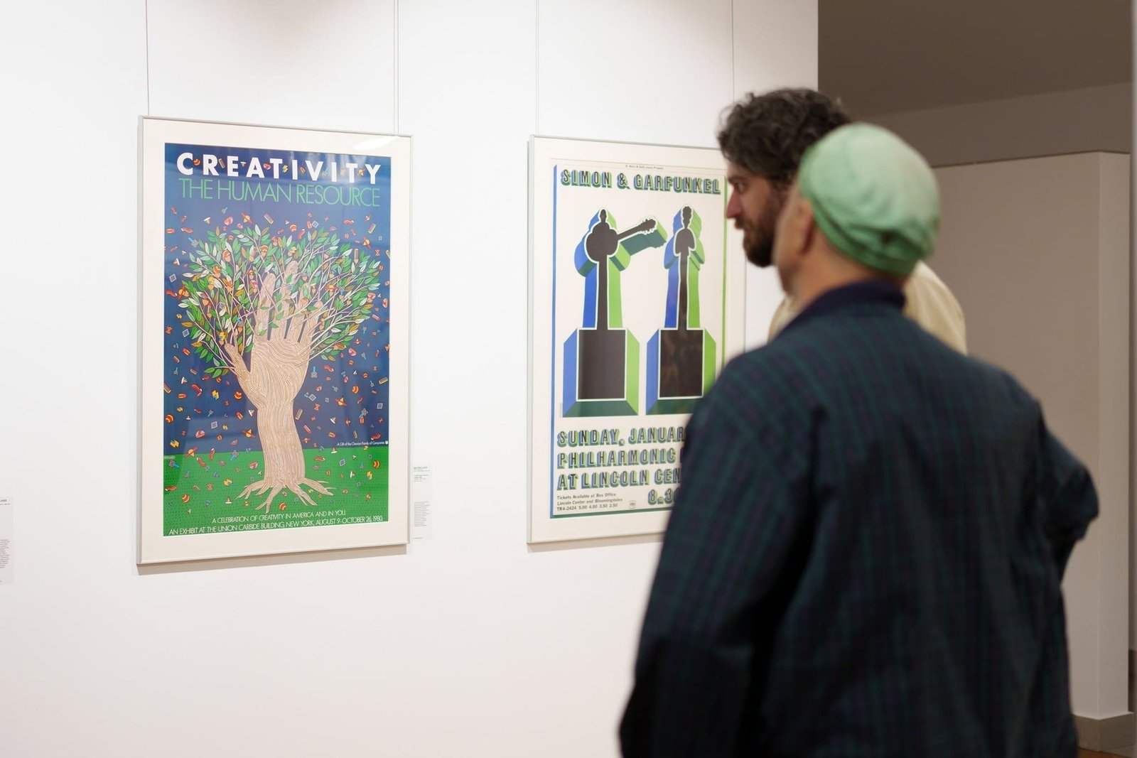Двое посетителей рассматривают постеры Милтона Глейзера «Creativity: The Human Resource» и «Simon & Garfunkel» на выставке в Кишинёве