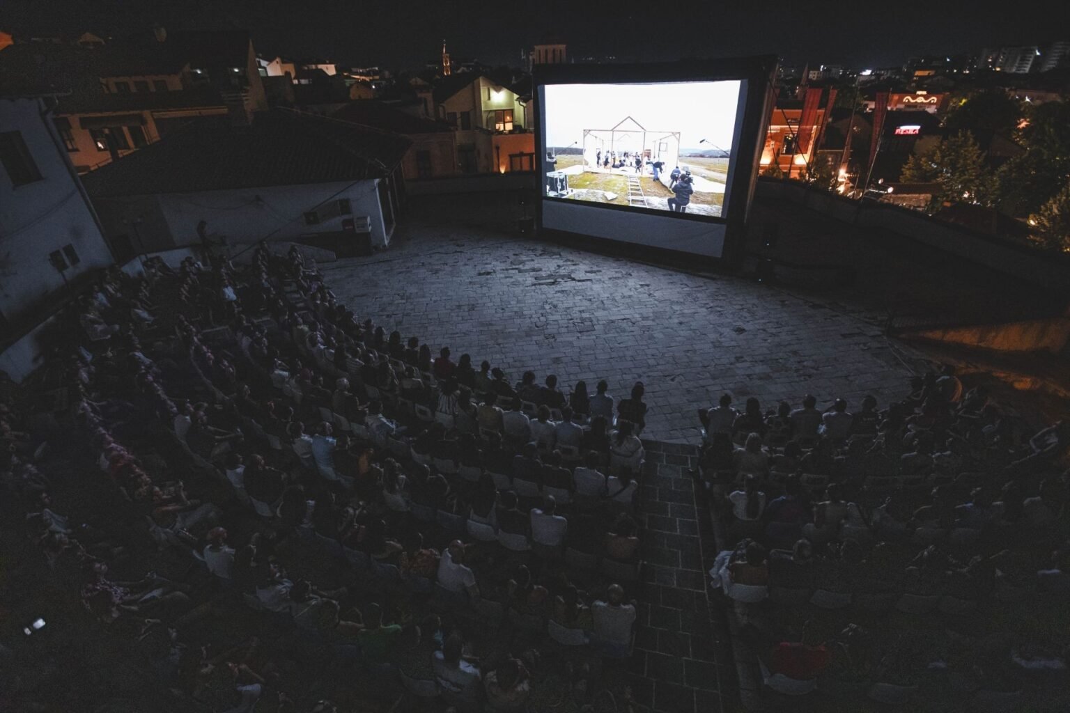 Ночной сеанс под открытым небом на площадке Kino Plato в Призрене: зрители заполнили каменный амфитеатр, а на большом экране идёт документальный фильм