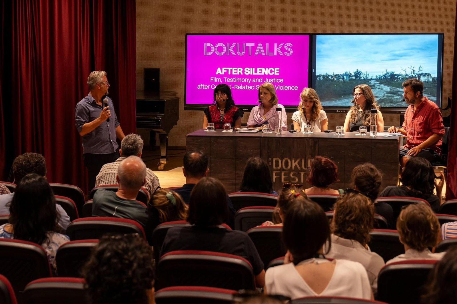 Дискуссия программы DokuTalks под заголовком &laquo;After Silence: Film, Testimony and Justice&raquo; &mdash; модератор с микрофоном и пять участниц панели перед полным залом фестивальной аудитории