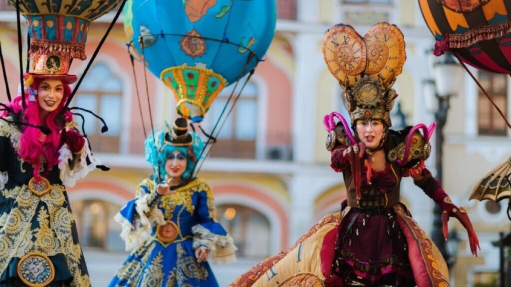 FestiFall 2026 в Орадя: финал с концертами и фейерверком Уличные артисты в костюмах с воздушными шарами и часовыми механизмами выступают на фоне исторических фасадов центра Орадя во время FestiFall 2026