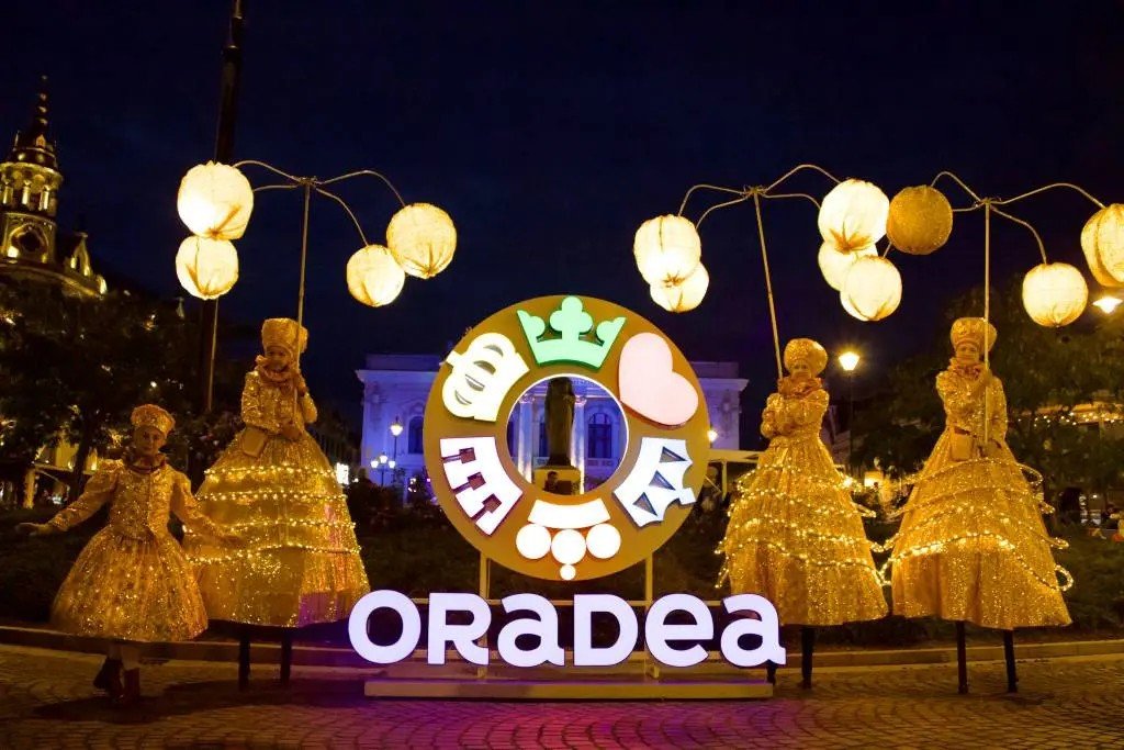 Инсталляция ORADEA с золотистыми светящимися шарами-фонарями и артистами в сверкающих костюмах в вечернем центре города во время FestiFall 2026