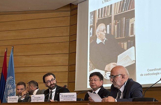 На экране в зале ЮНЕСКО — архивный портрет Грачия Ачаряна за рабочим столом в библиотеке: кадр из презентации на пленарной сессии